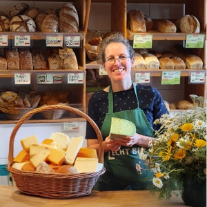 Karoline aus unserem Hofladen hält Käse. Im Hintergrund sind viele Brote.