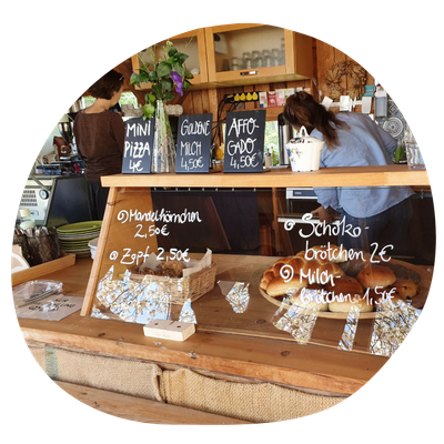 KI generiert: Kaffeehaus-Theke mit Gebäck und Schildern; Produkte: Mini Pizza, Goldene Milch, Affogato. Preise: 2€ bis 4,50€.