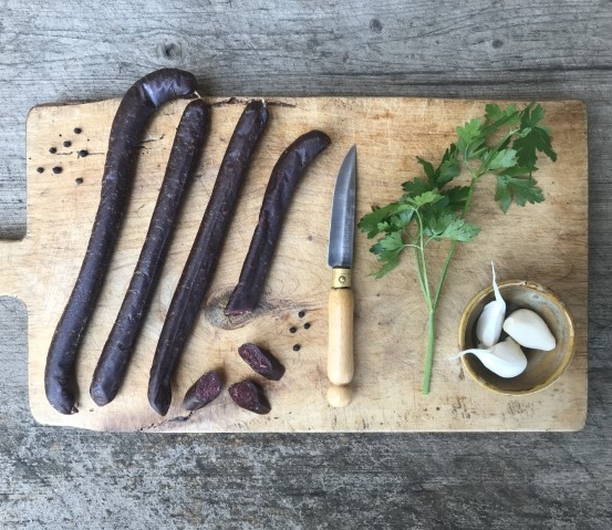 Wurststücke, ein Messer, Petersilie und Knoblauch auf einem Holzbrett.