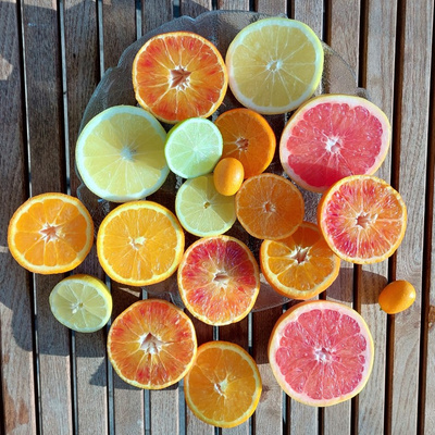 KI generiert: Das Bild zeigt eine Vielzahl von aufgeschnittenen Zitrusfrüchten, darunter Orangen, Grapefruits, Limetten, Zitronen und Kumquats, die auf einem Holztisch arrangiert sind. Die farbenfrohen Fruchtscheiben bilden ein lebendiges und ansprechendes Stillleben.