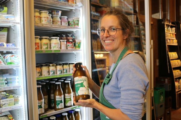 Hofladenmitarbeiterin Karoline steht vor einem Kühlschrank in unserem Hofladen und hält eine Flasche Vollmilch in der Hand.