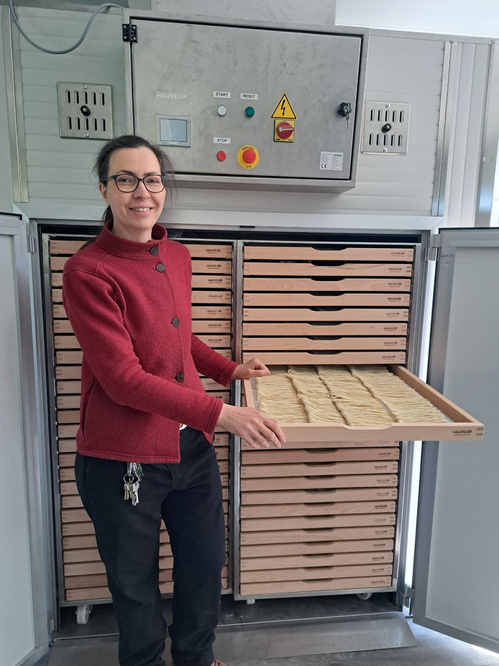 KI generiert: Eine Frau präsentiert ein Tablett mit Teig in einem Trockenschrank. Text auf Gerät: "HÄUSSLER".