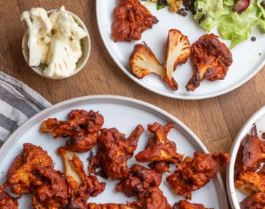 Gebackener Blumenkohl in BBQ-Soße auf Tellern mit Salat und rohem Blumenkohl in einer Schale.