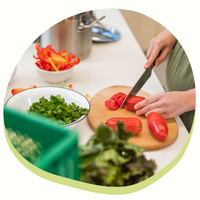 KI generiert: Eine Person schneidet frische rote Paprika auf einem Schneidebrett. Auf dem Tisch liegen weitere Zutaten wie gehackte Kräuter und geschnittene Paprika in Schalen.