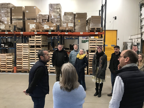 KI generiert: Gruppe von Menschen in einer Lagerhalle bei einer Führung oder Besprechung.