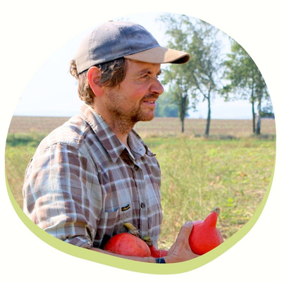 KI generiert: Das Bild zeigt einen Mann auf einem Feld, der mehrere Kürbisse in den Armen hält. Der Hintergrund besteht aus einer offenen Landschaft mit Bäumen.