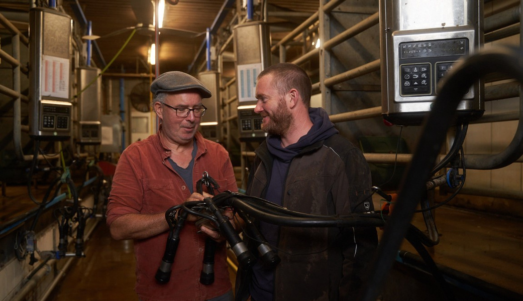 KI generiert: Zwei Männer in einer Molkerei mit Melkgerät, lächelnd.